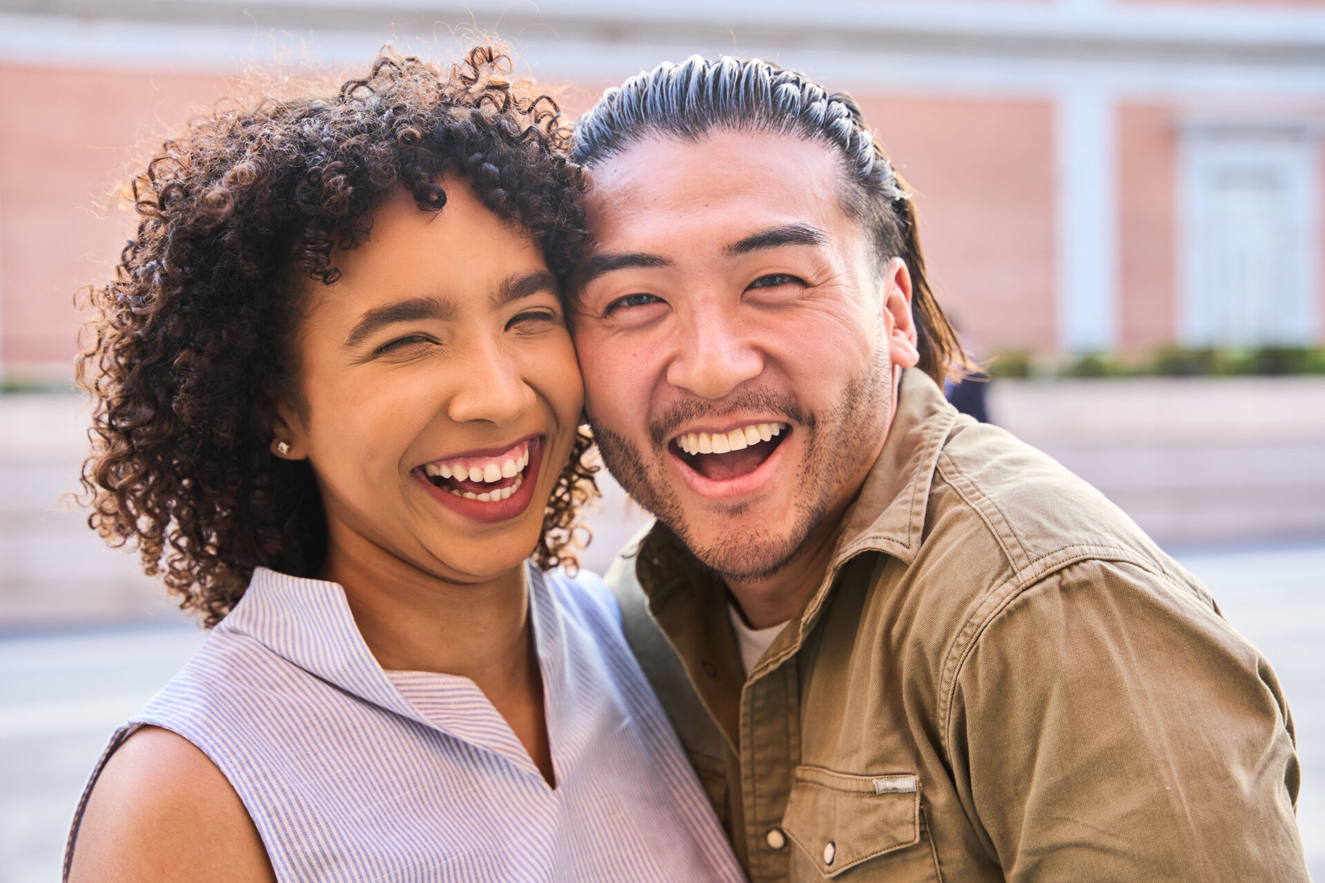 Young multi ethnic couple laughing joyfully while enjoying each other's company in a vibrant urban setting, radiating happiness and love